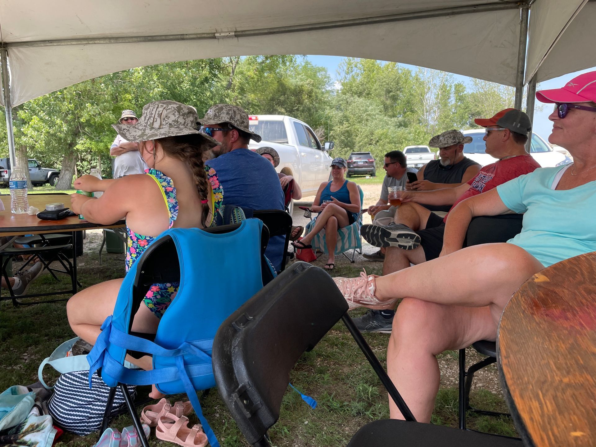 Adults are sitting at a table under a large white tent.