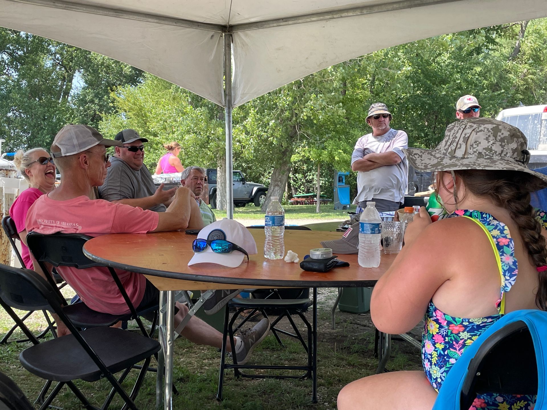 Adults are sitting at a table under a large white tent.