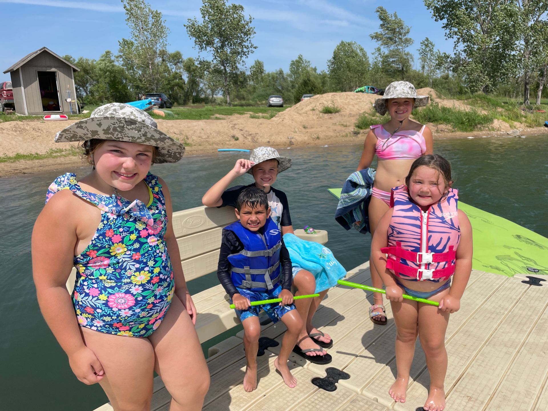 Cute kids are in their swimsuits and smiling at the camera by a lake.