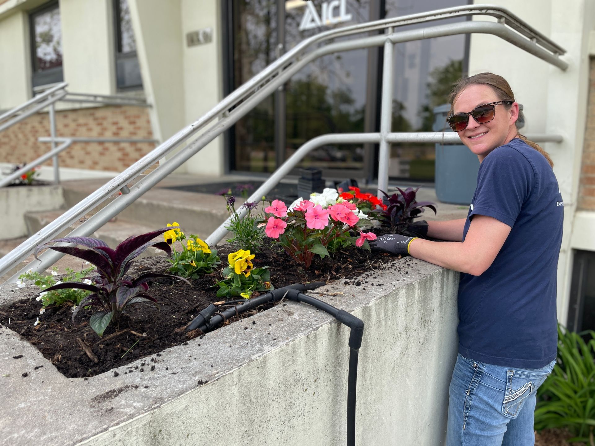 an icl employee is standing next to a planter with flowers in front of a building .