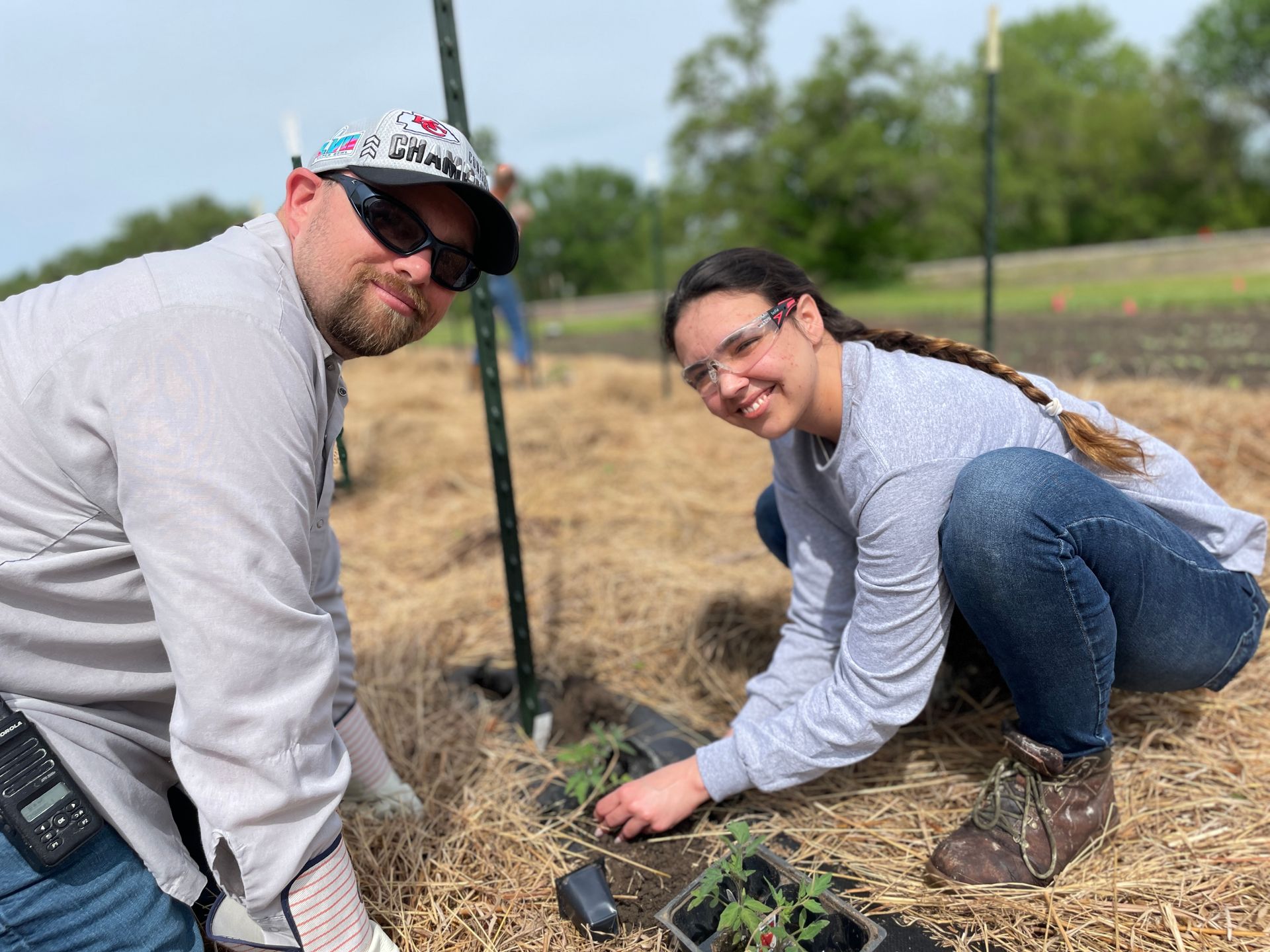 Two people are squatting as they plant plants for the ICL Spring Plant.