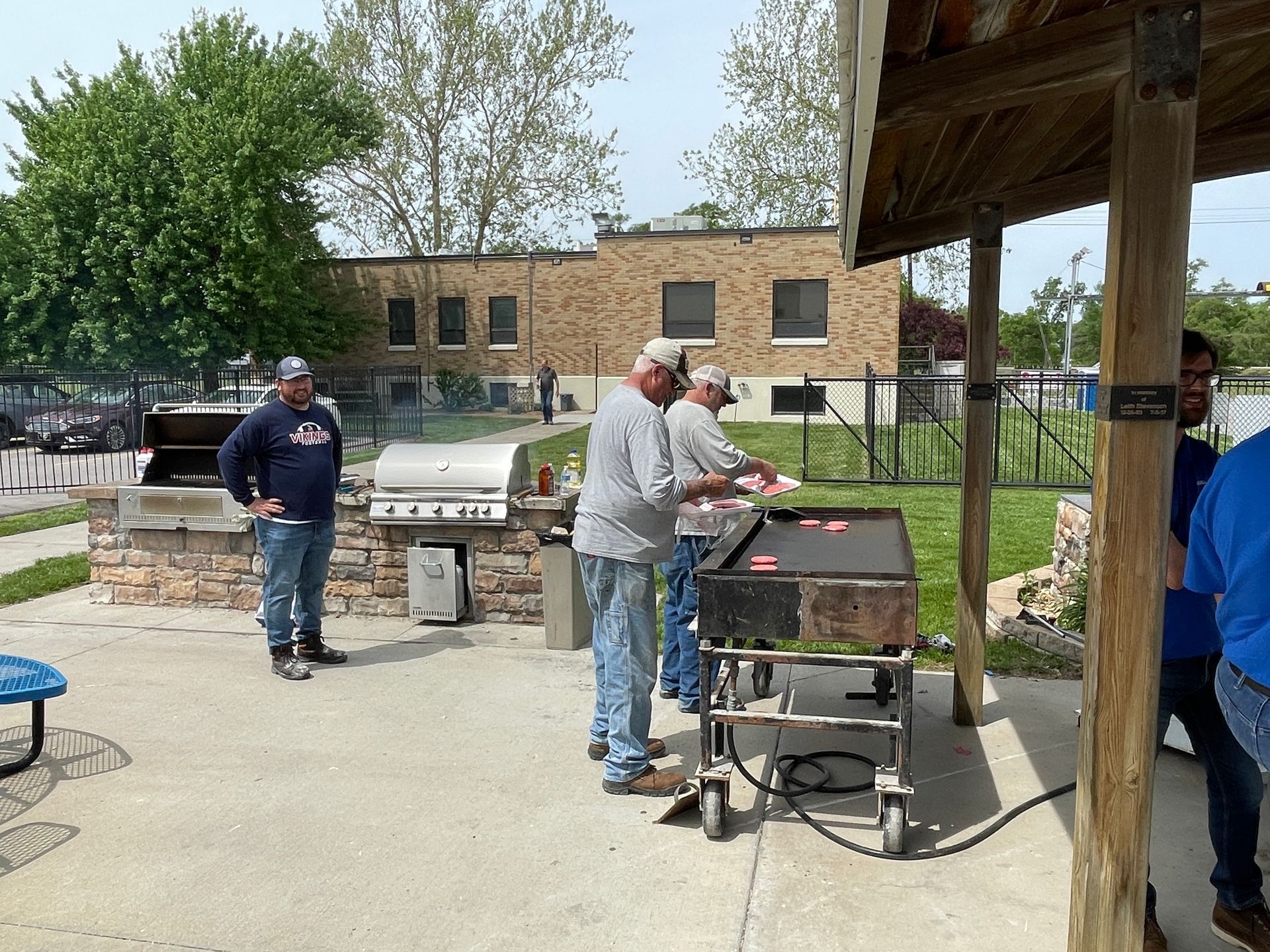 People are standing on a patio around a large grill.