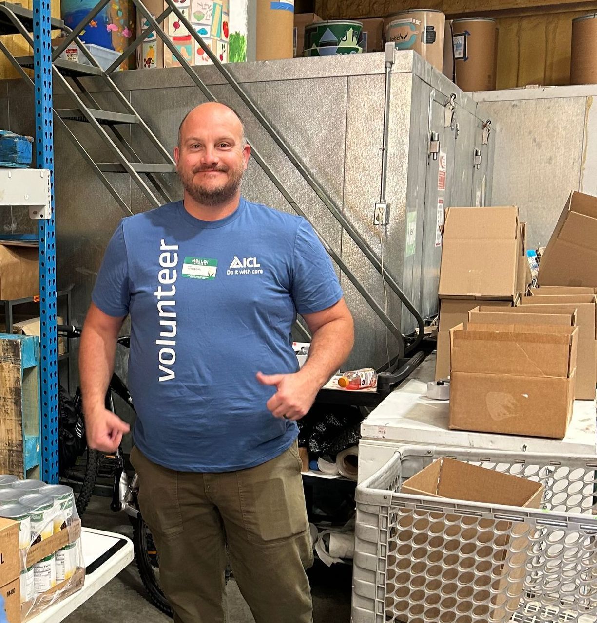 an icl employee  wearing a blue volunteer shirt is standing in a warehouse