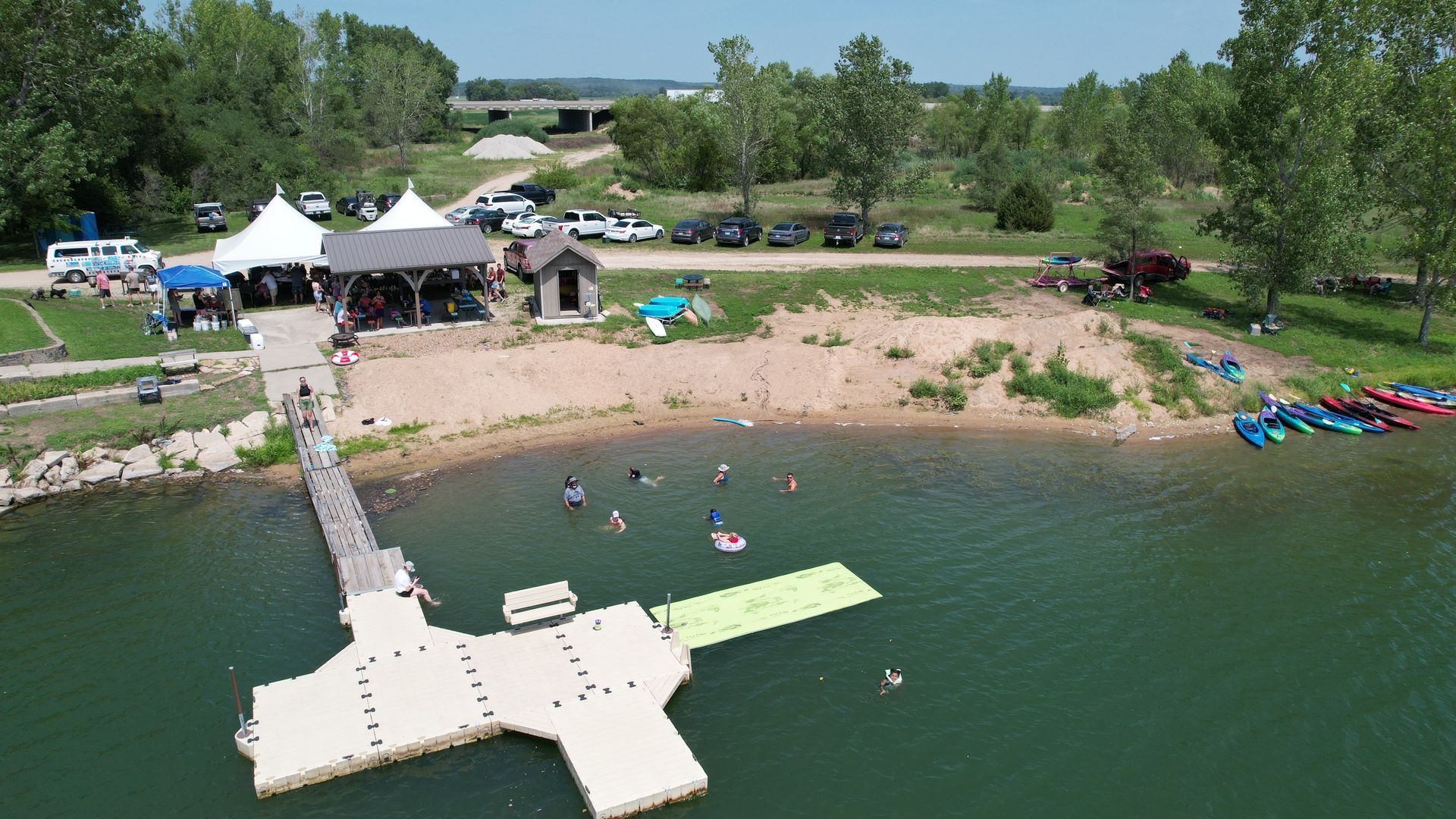 Arial view of the lake with a beach, dock and the large white tents.