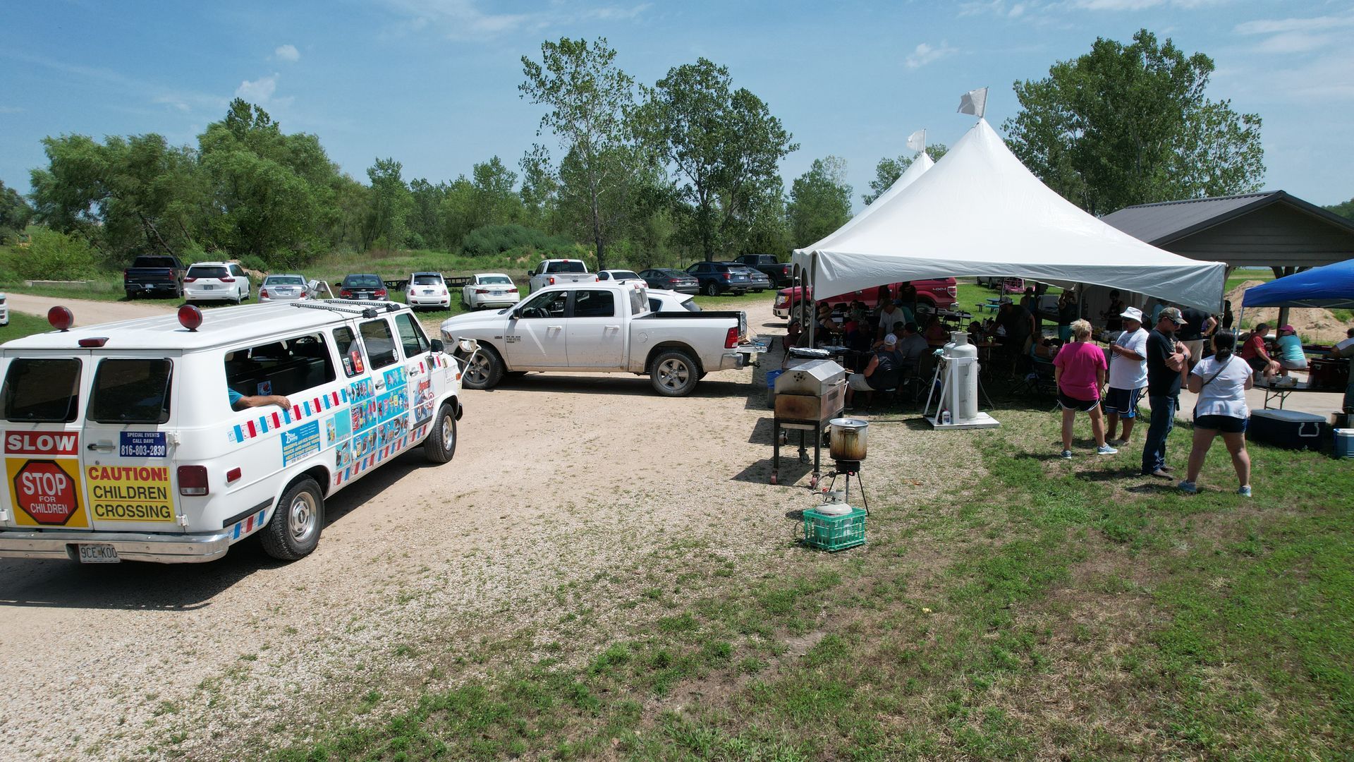 View of the picnic party with cars and tents with people walking around.