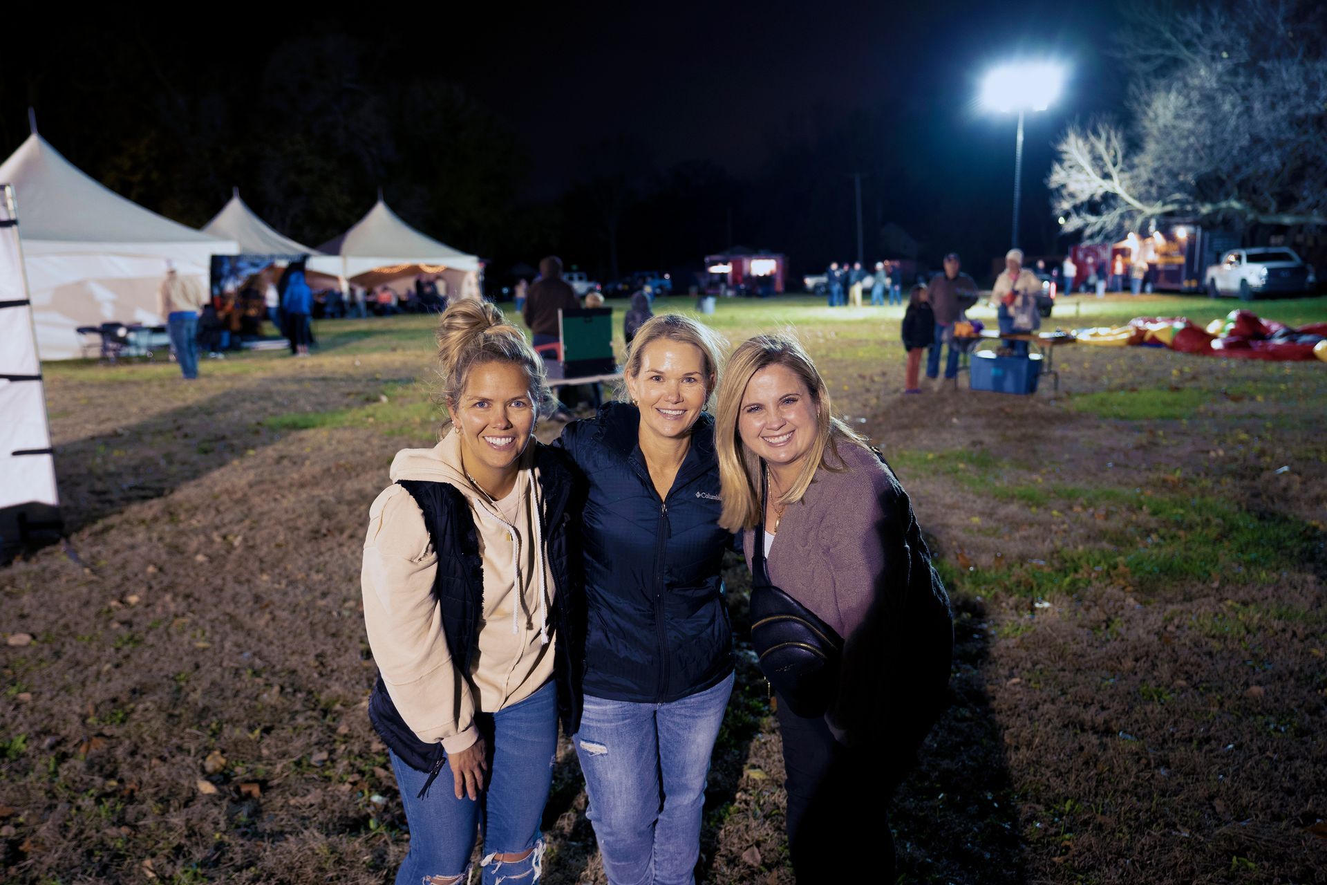 Three women are posing for a picture in a field at night.