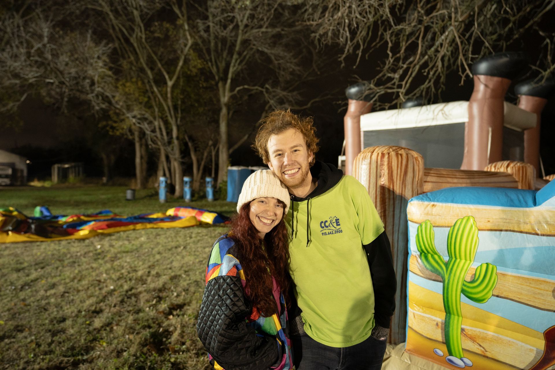 A man and a woman are posing for a picture in front of a bouncy house.
