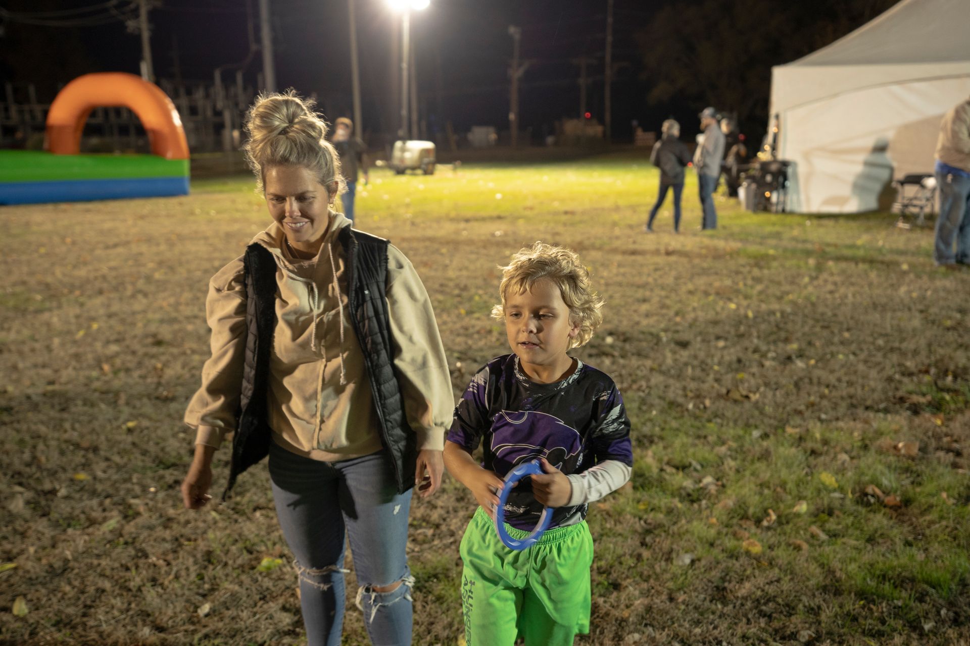 A woman and a child are walking in a field at night.