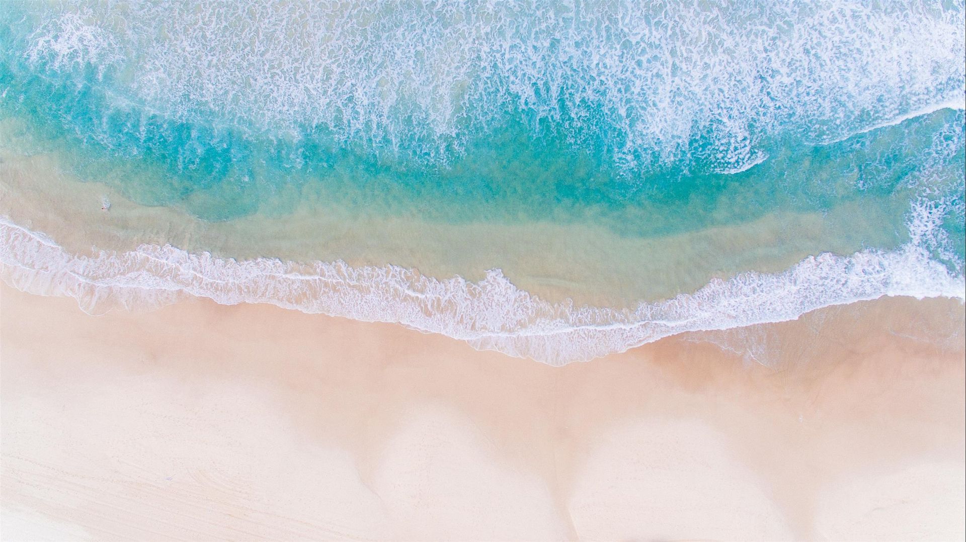 An aerial view of a beach with waves crashing on the sand.