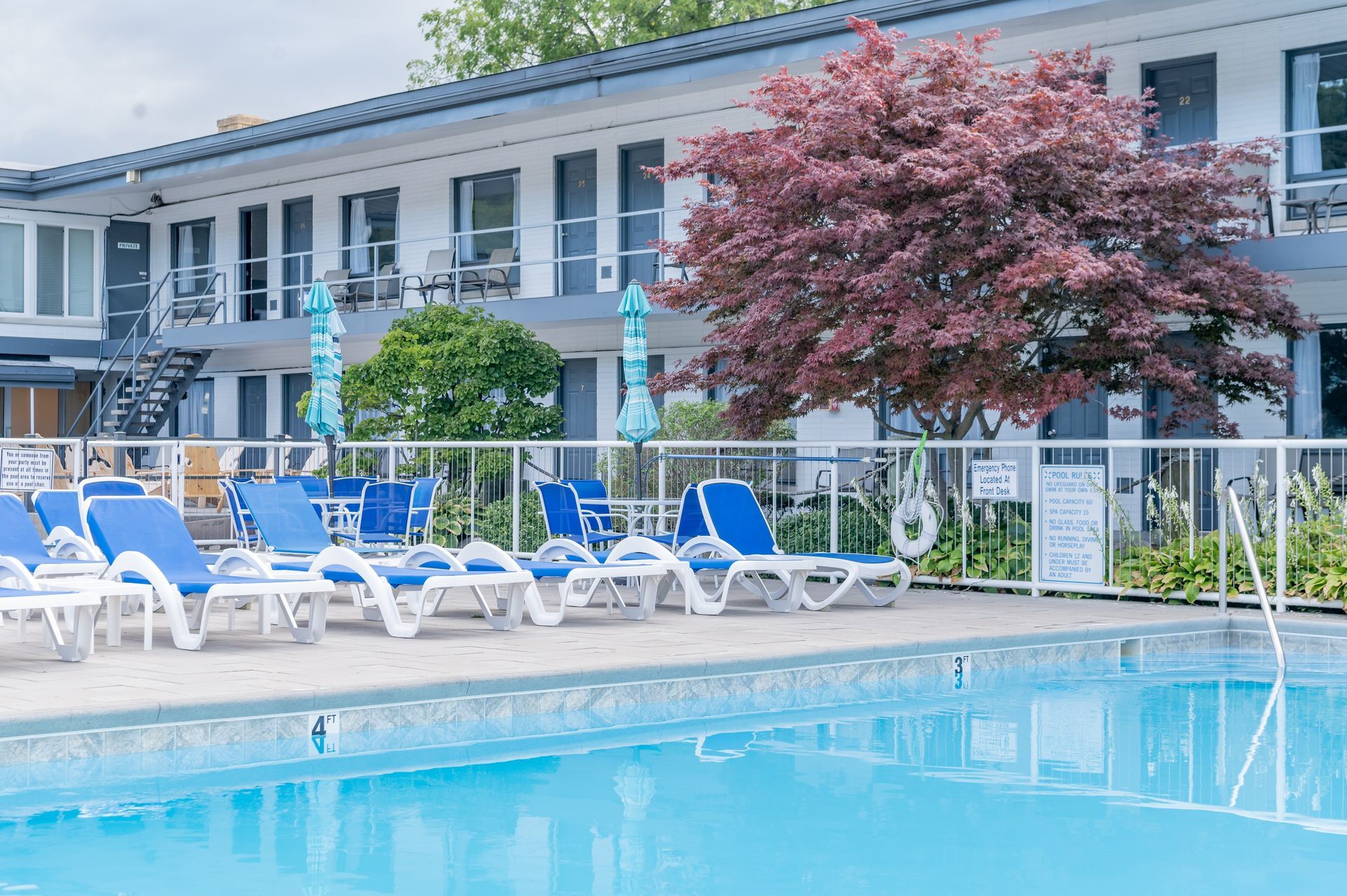 A large swimming pool surrounded by chairs and umbrellas in front of a hotel.