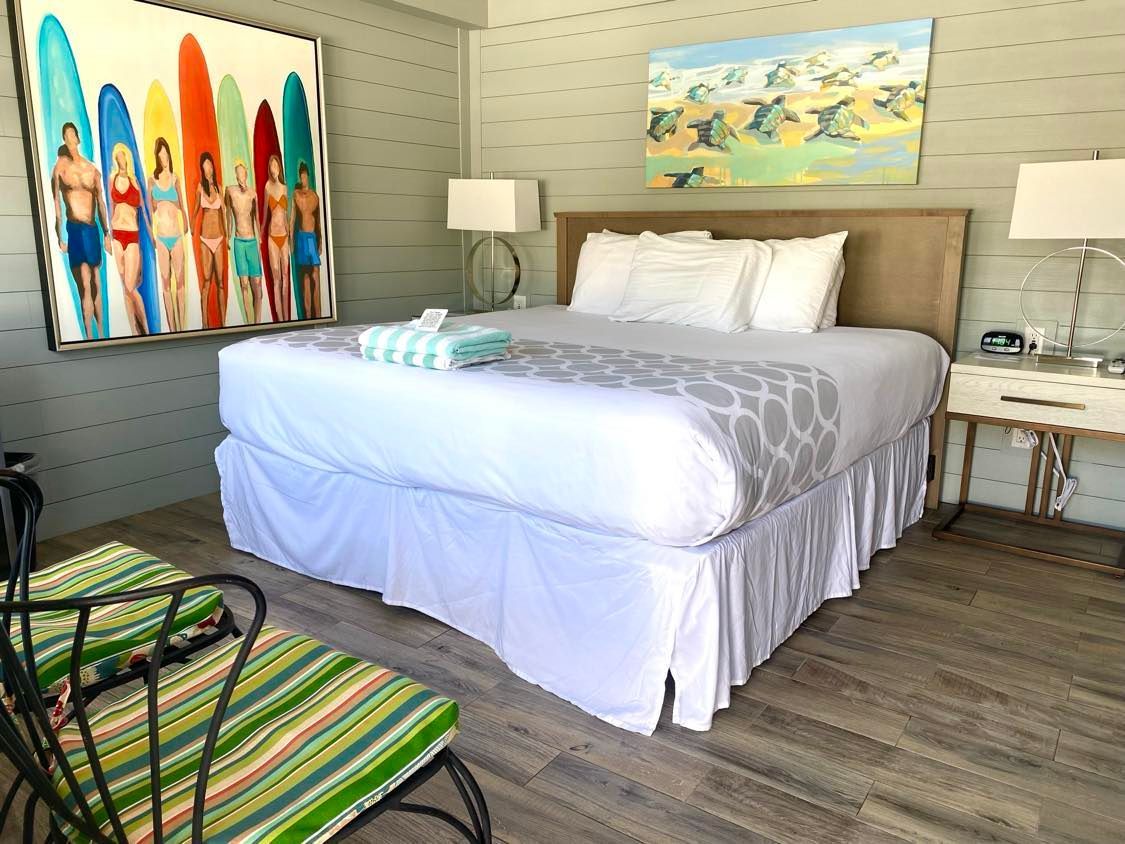 A hotel room with a large bed and a painting of surfboards on the wall.