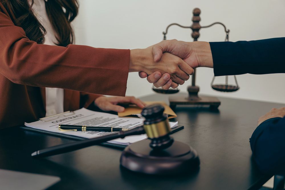 Persona con chaqueta marrón estrechando la mano de otra persona en un escritorio