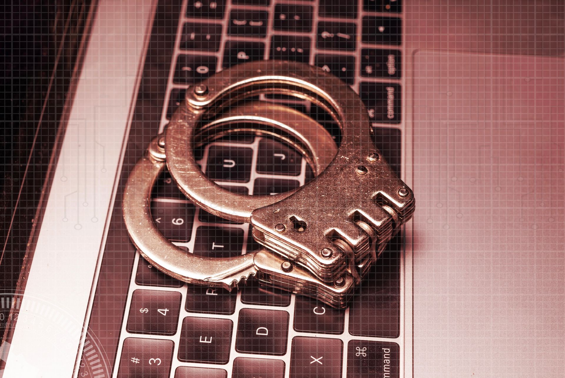 Esposas en un teclado de computadora portátil, tono rojo que sugiere delito cibernético.