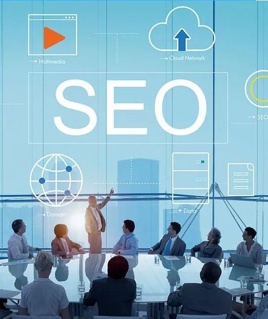 Business meeting discussing SEO strategy; people around a table looking at the presenter who points to a digital graphic of a cloud, globe, and multimedia icons.