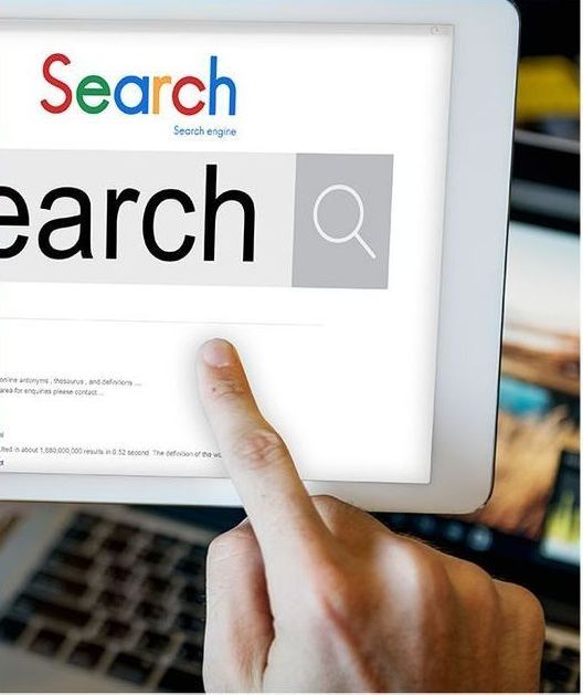 Person's finger touching a tablet screen displaying a search bar on a website. The word 