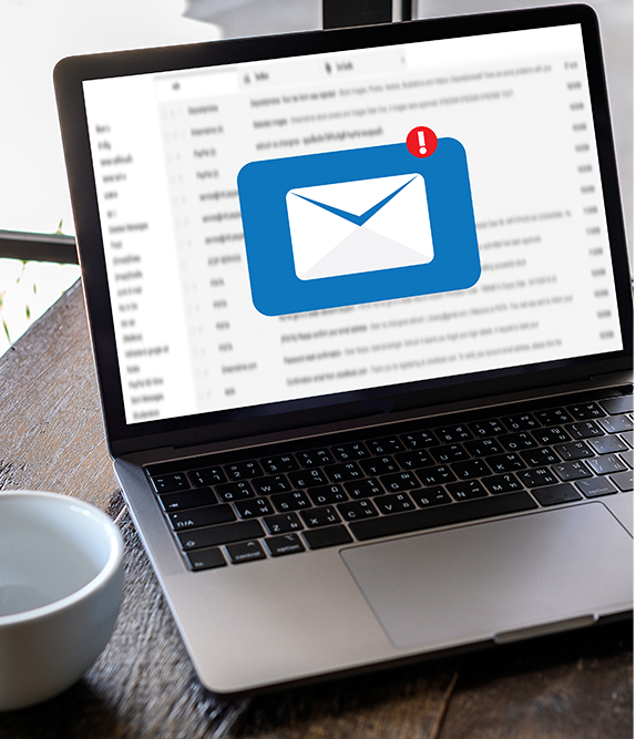Laptop displaying an email inbox with a blue notification icon, next to a white coffee cup.
