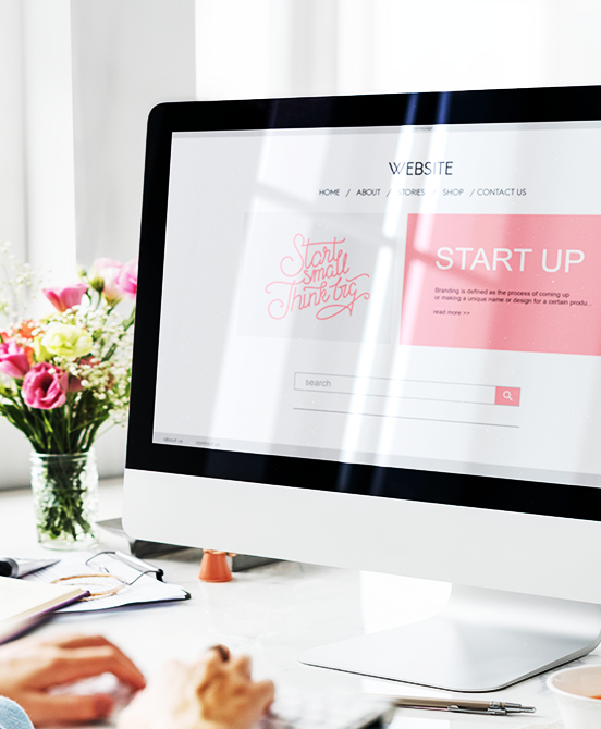 A person using a computer showing a website design with pink accents, a floral arrangement, and bright lighting.