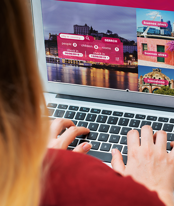 Person typing on a laptop, website with travel destination search interface on screen.  Rose-colored interface and photos are prominent.