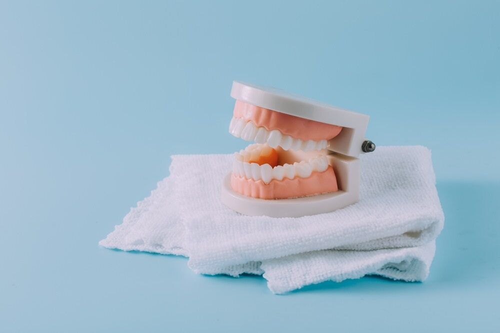 A Model Of Teeth Is Sitting On A White Towel On A Blue Background — Dentures Direct Taree-Rod Hinton In Wauchope, NSW