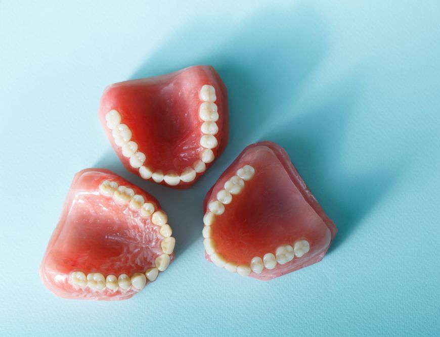 Three Dentures Are Sitting On A Blue Surface — Dentures Direct Taree-Rod Hinton In Port Macquarie, NSW