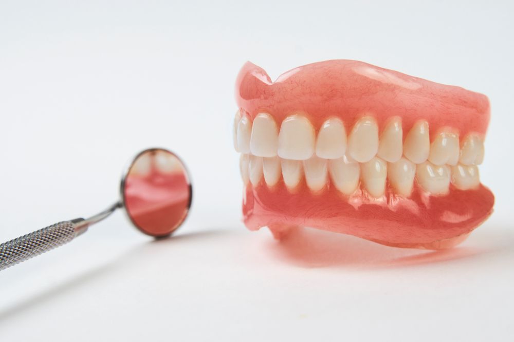 A Denture And A Dental Mirror On A White Surface — Dentures Direct Taree-Rod Hinton In Taree, NSW
