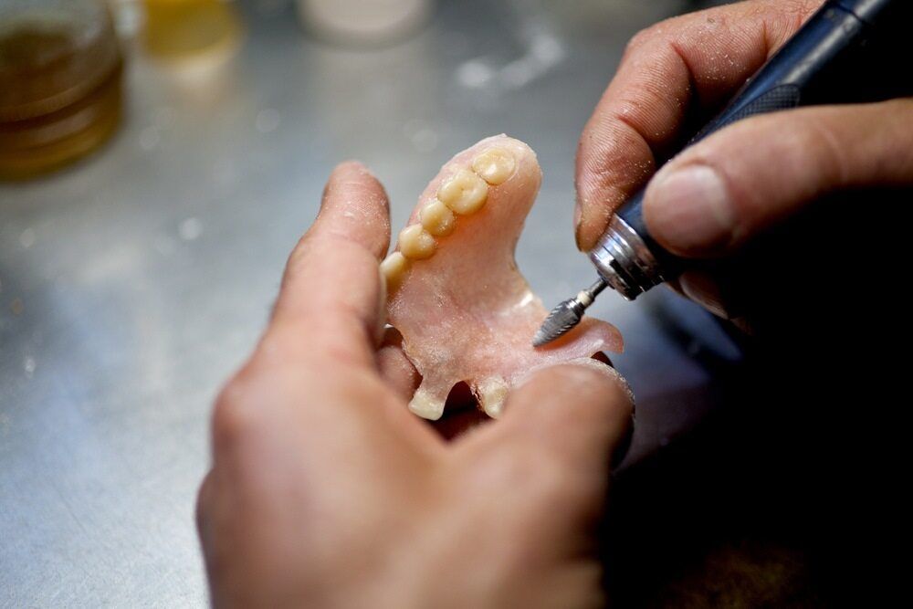 A Person Is Working On A Denture With A Machine — Dentures Direct Taree-Rod Hinton In Wauchope, NSW
