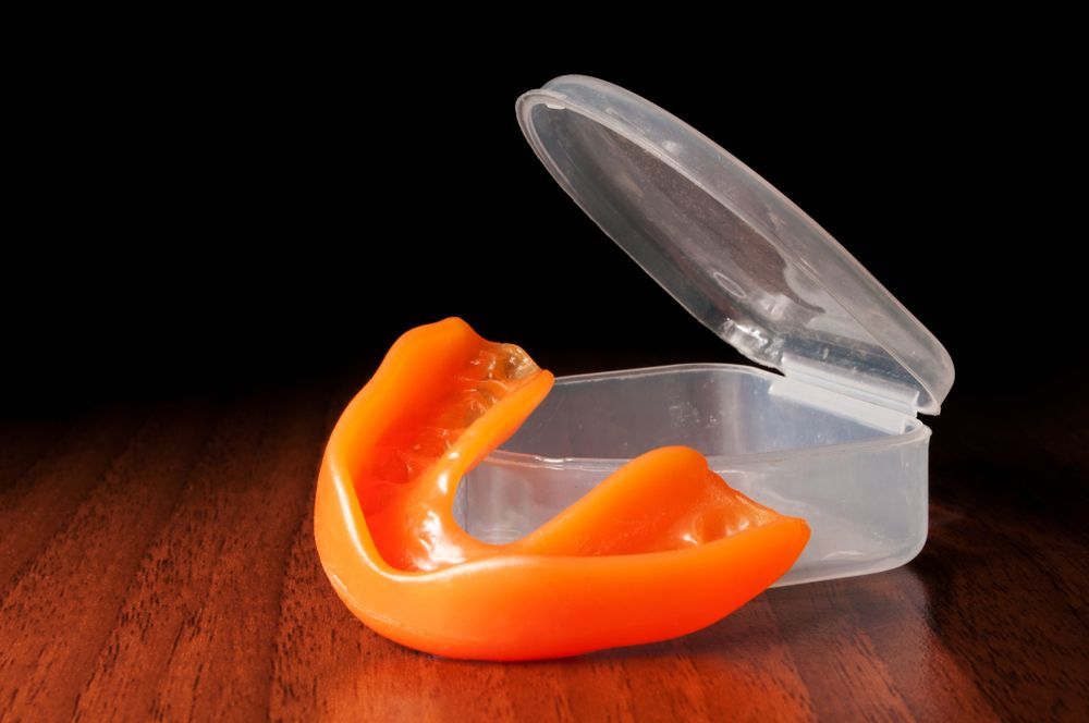 An orange mouth guard is sitting in a plastic case on a wooden table.