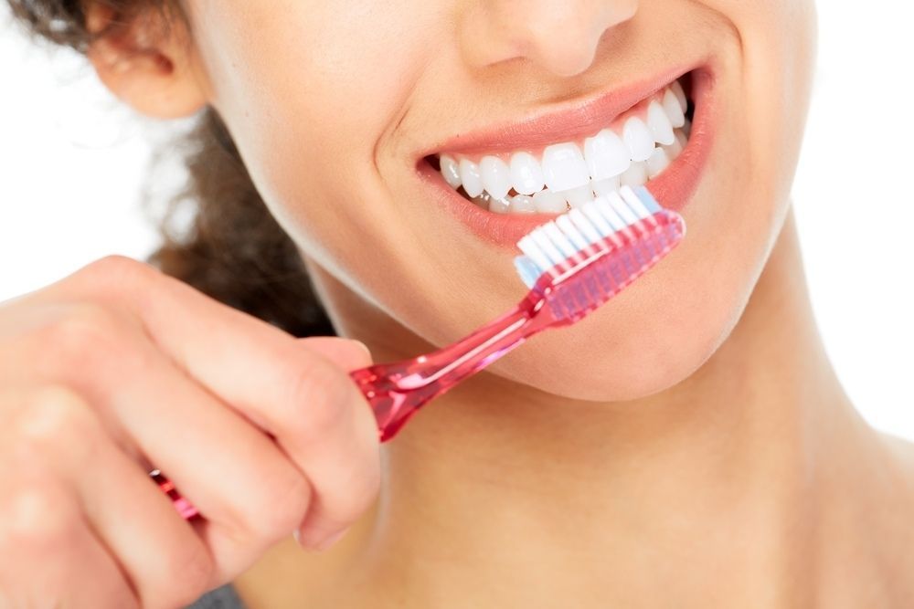 A Woman Is Brushing Her Teeth With A Pink Toothbrush — Dentures Direct Taree-Rod Hinton In Taree, NSW