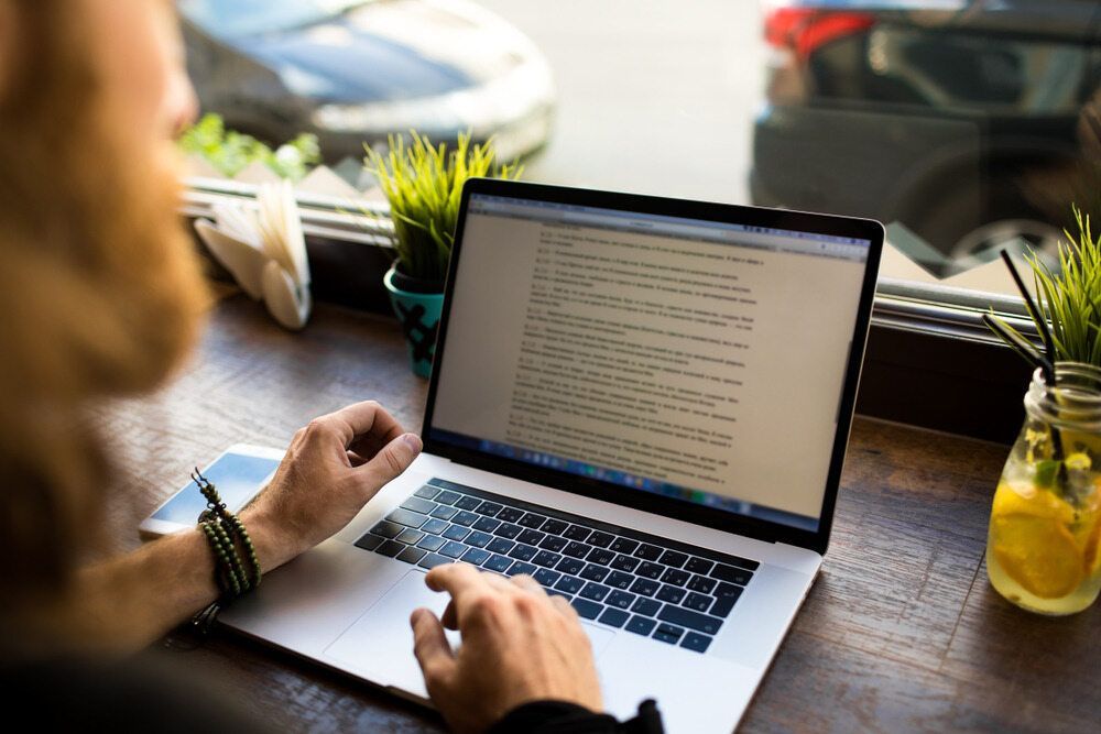A Man Is Typing On A Laptop Computer While Sitting At A Table — Dentures Direct Taree-Rod Hinton In Taree, NSW