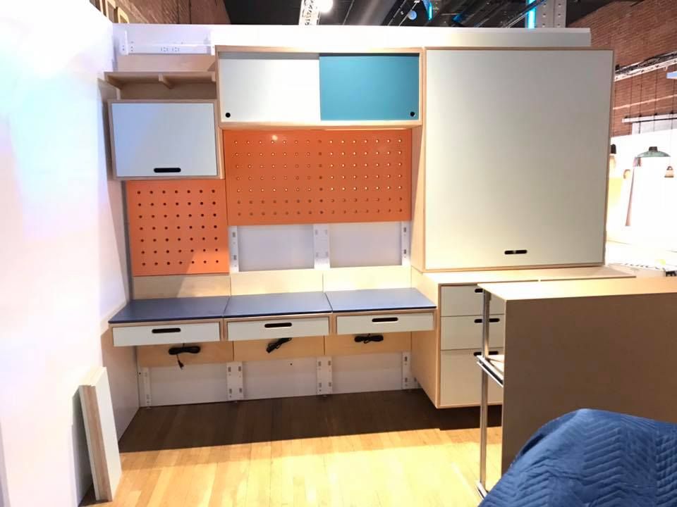 Built-in desk with storage, drawers, and pegboard against a light-colored wall, illuminated indoors.