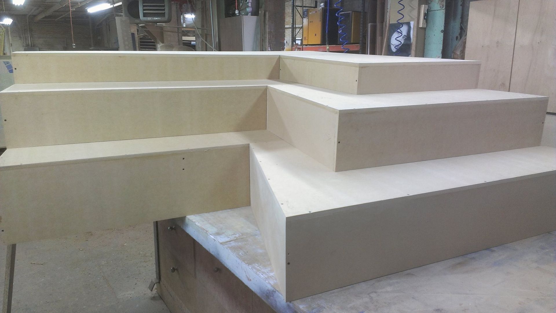 L-shaped wooden steps, beige color, inside a workshop, with varying step heights.