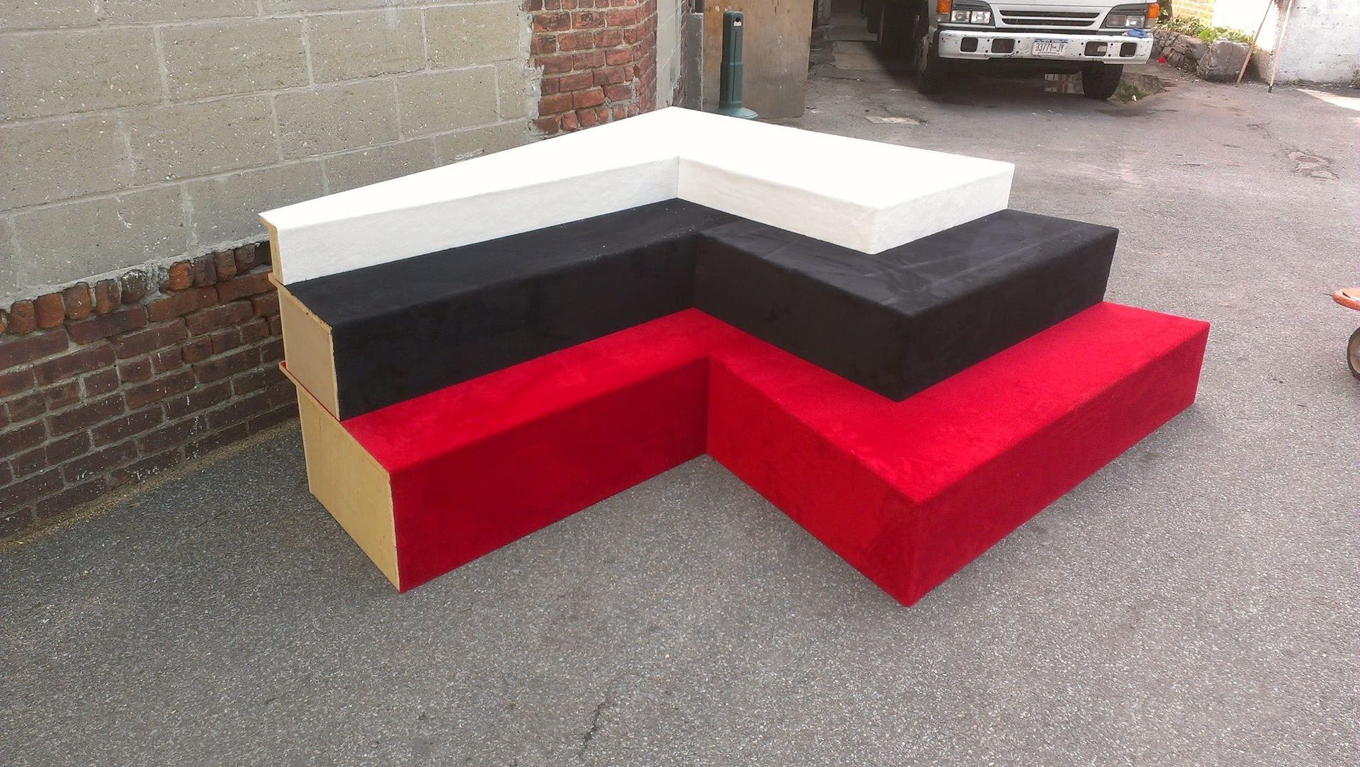 L-shaped tiered display platform, red, black, and white, on asphalt.