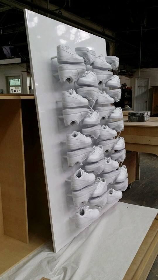 White sneakers arranged on a white vertical display in a workshop, showcasing a shoe collection.