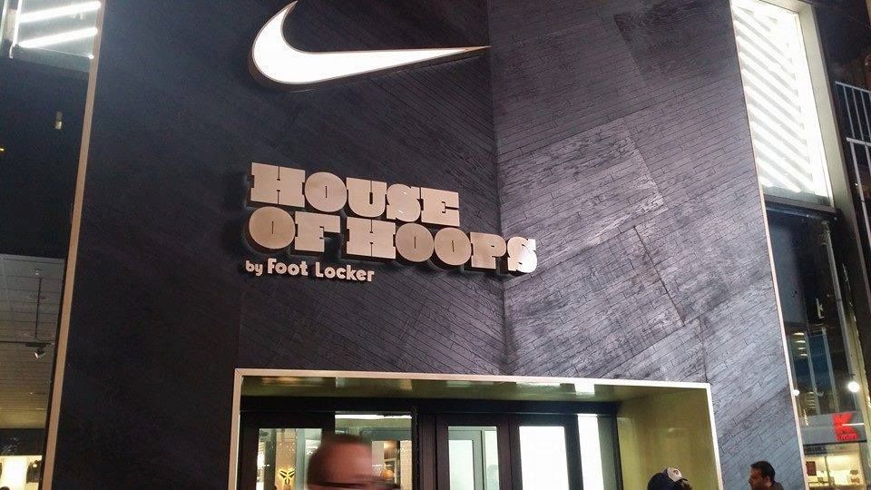 Exterior of a Nike House of Hoops store by Foot Locker, with black facade, large Nike swoosh, and entrance.