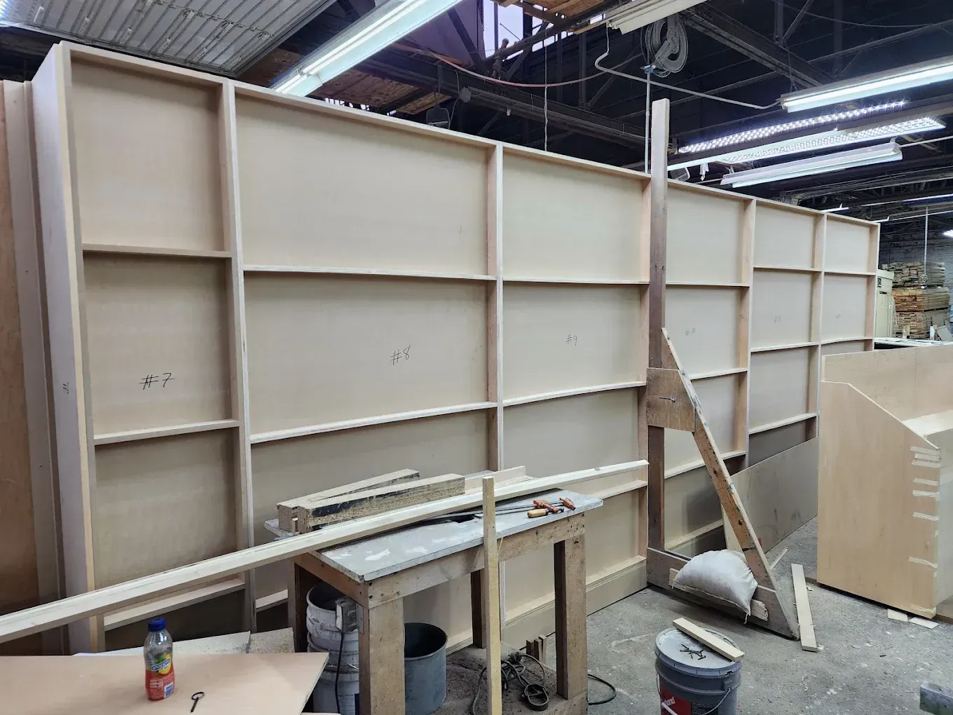 Wooden wall under construction in a workshop, with supports, tools, and unfinished panels.