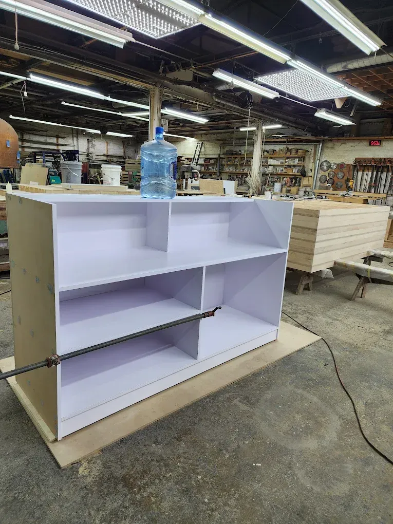 White bookshelf with dividers, blue water jug on top, in a workshop setting.