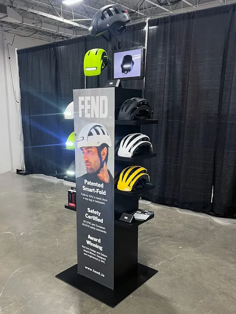 Display of FEHD helmets on shelves; man's face on promotional signage. Black and yellow helmets visible.