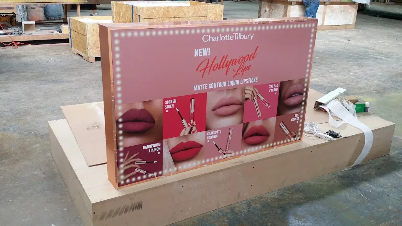 Large makeup box on a cardboard platform. Pink and gold, with images of lips. Warehouse setting.