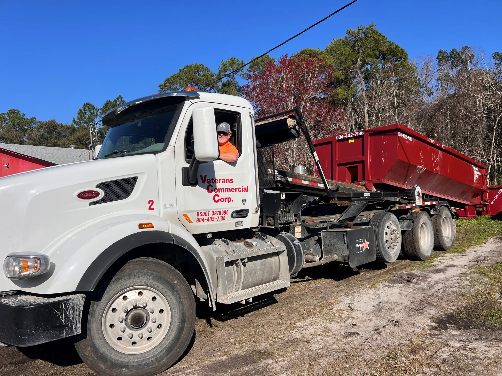 A white dump truck is parked next to a red dumpster.