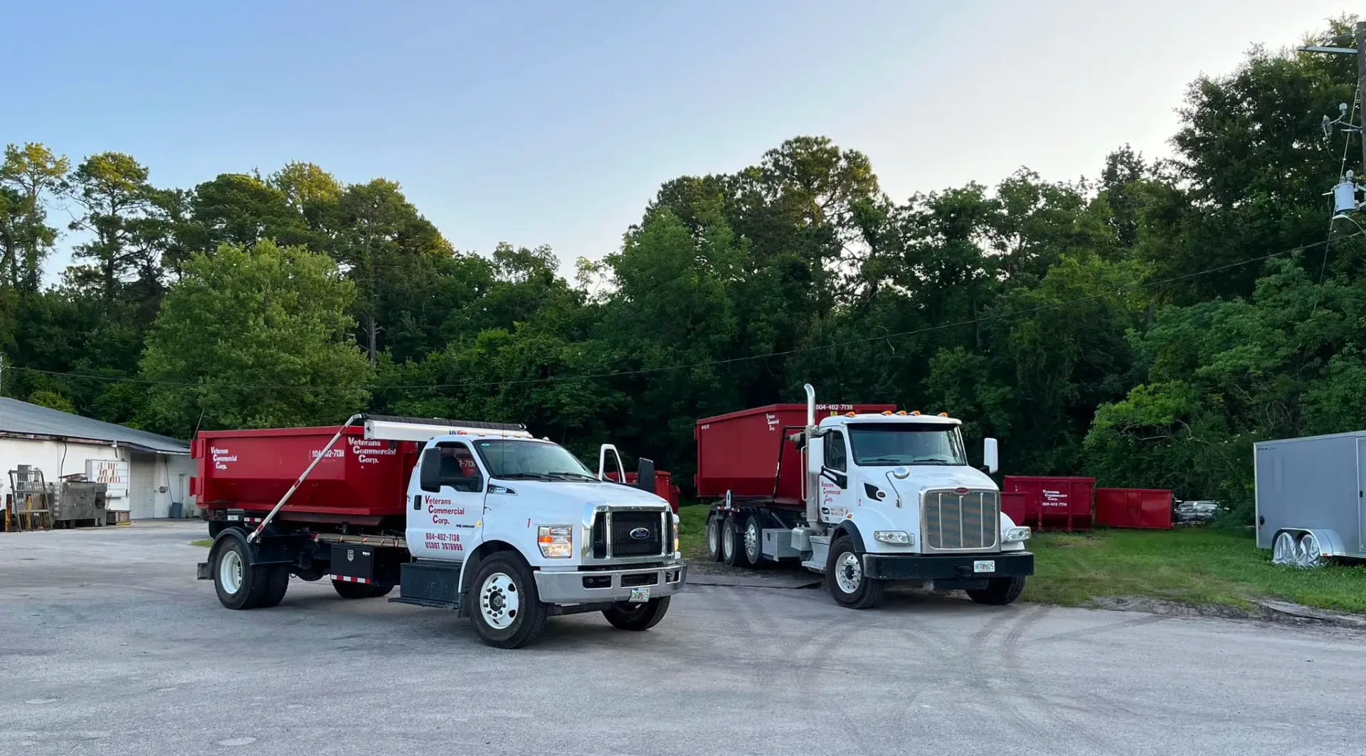 A dumpster is being towed by a dump truck in a driveway.