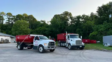 A green dumpster is sitting in a warehouse next to a truck.
