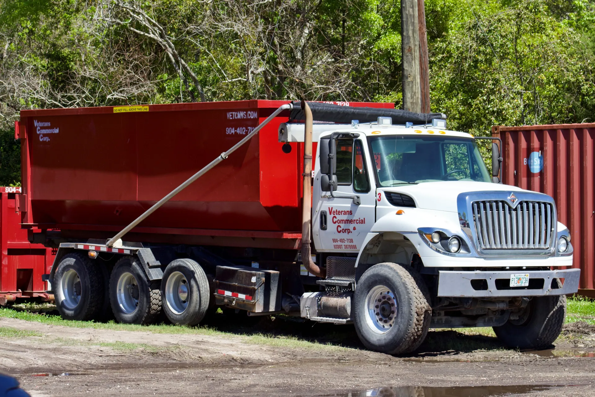 A dumpster is being towed by a dump truck in a driveway.