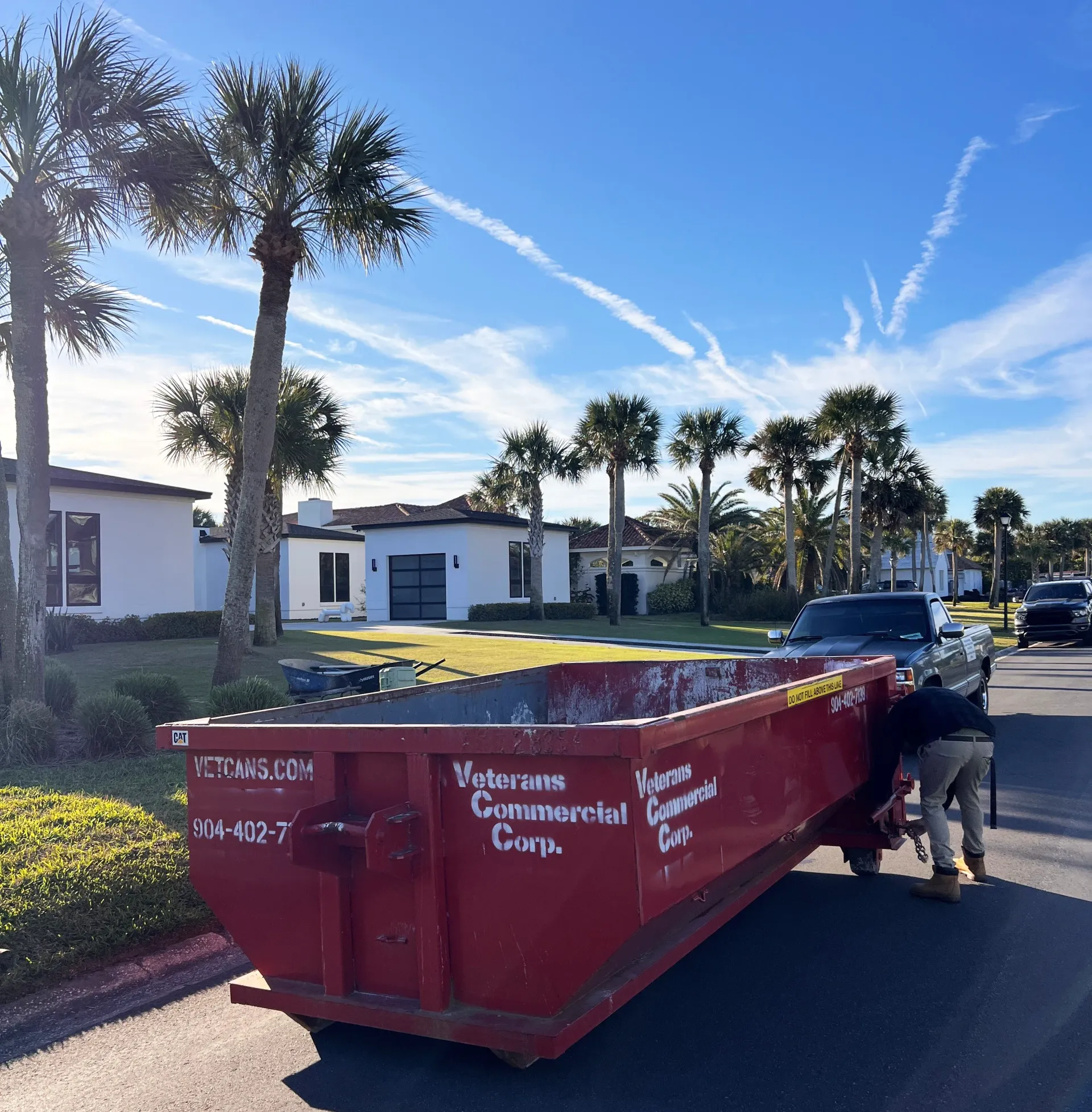 A green dumpster is sitting on the side of a truck in front of a house.
