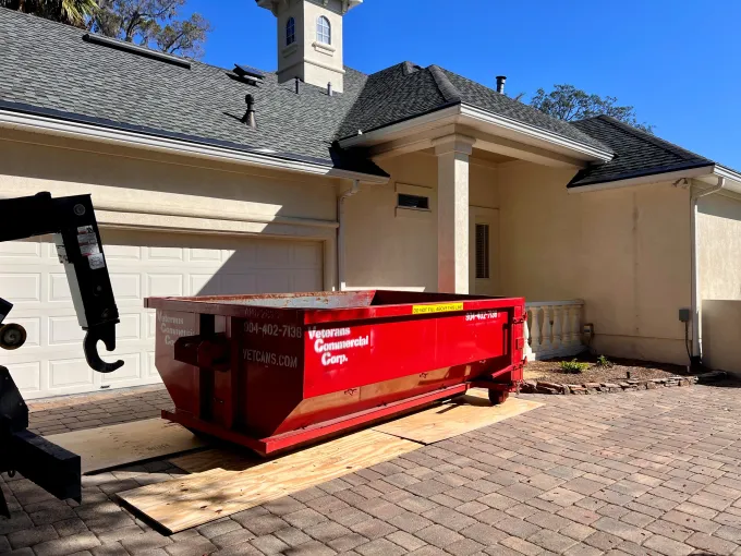 A green dumpster is parked in front of a house.