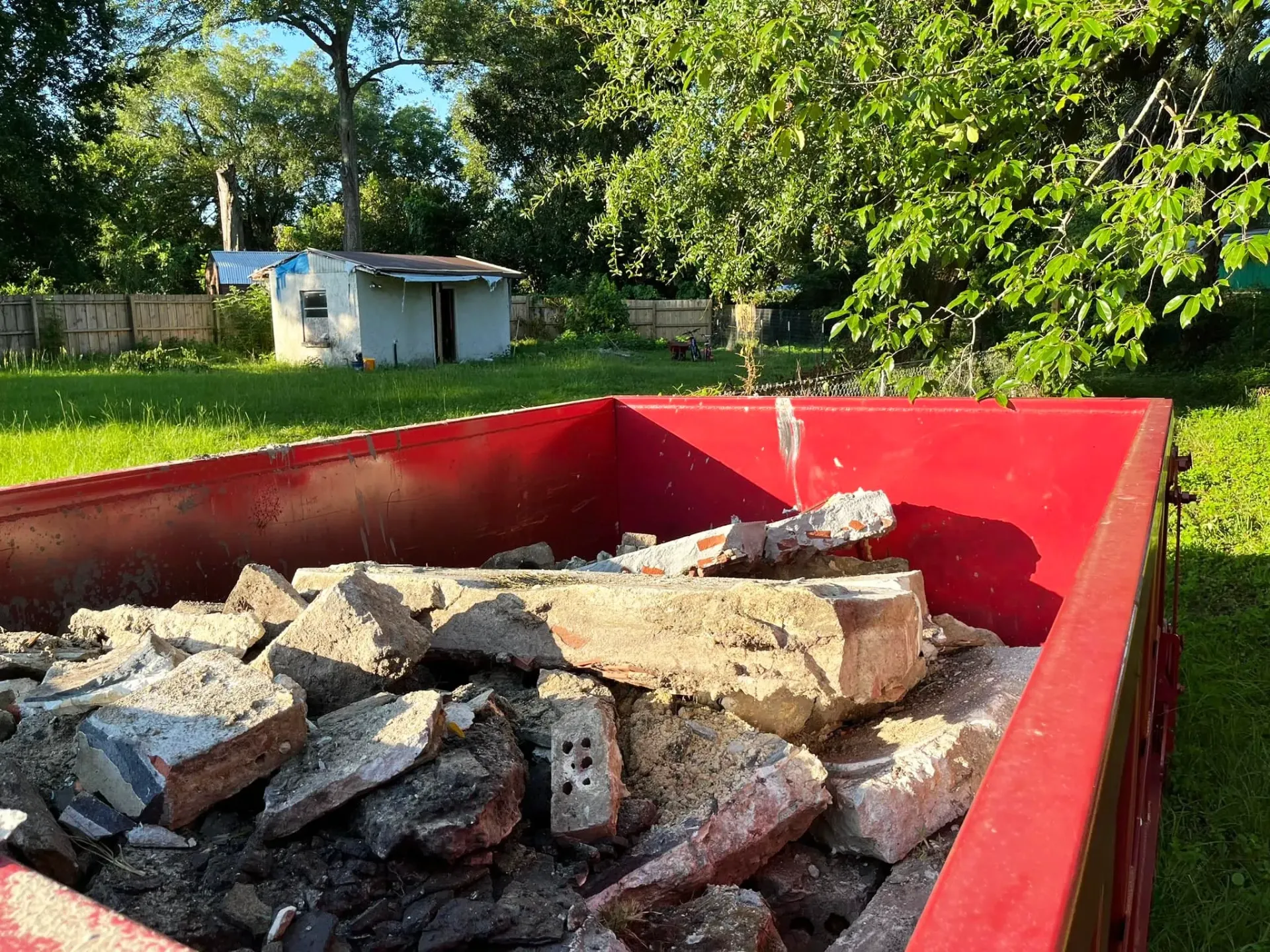 A dumpster is being towed by a dump truck in a driveway.