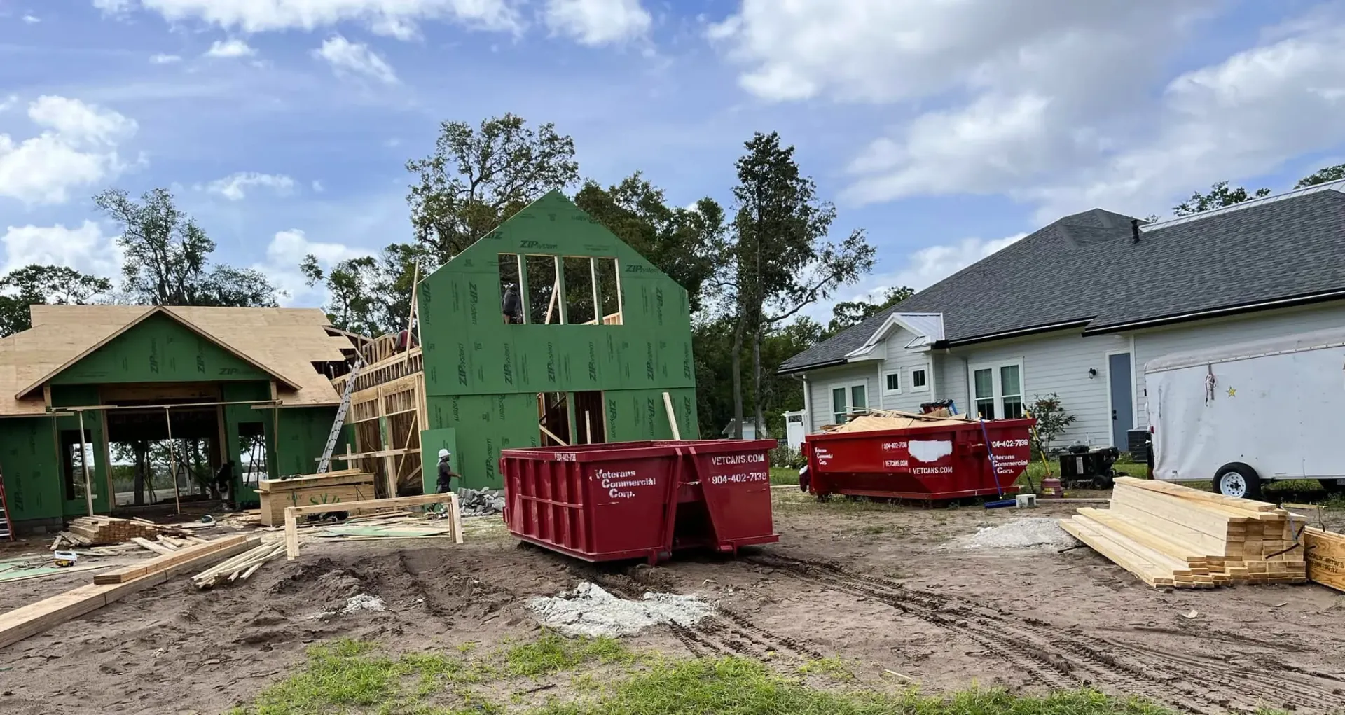 A green dumpster filled with wood is parked in front of a house.