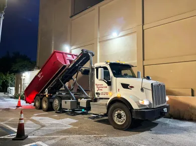 A green dumpster is parked in front of a rose nail salon.