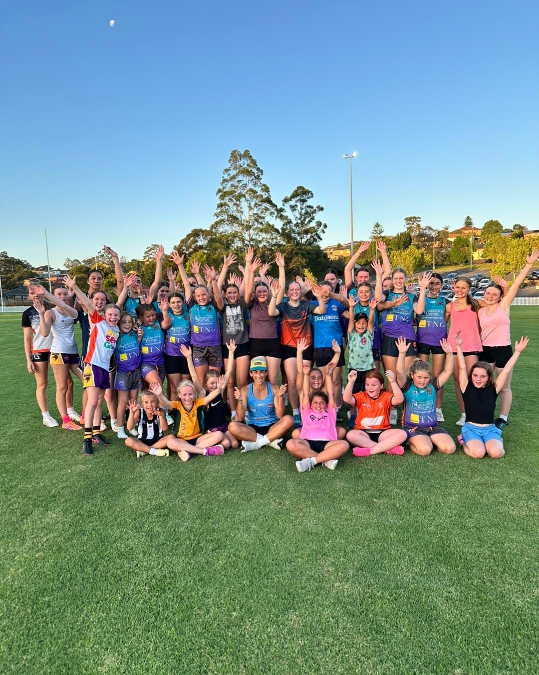 Group of people on a green field with arms raised in the air. They are wearing athletic clothing.