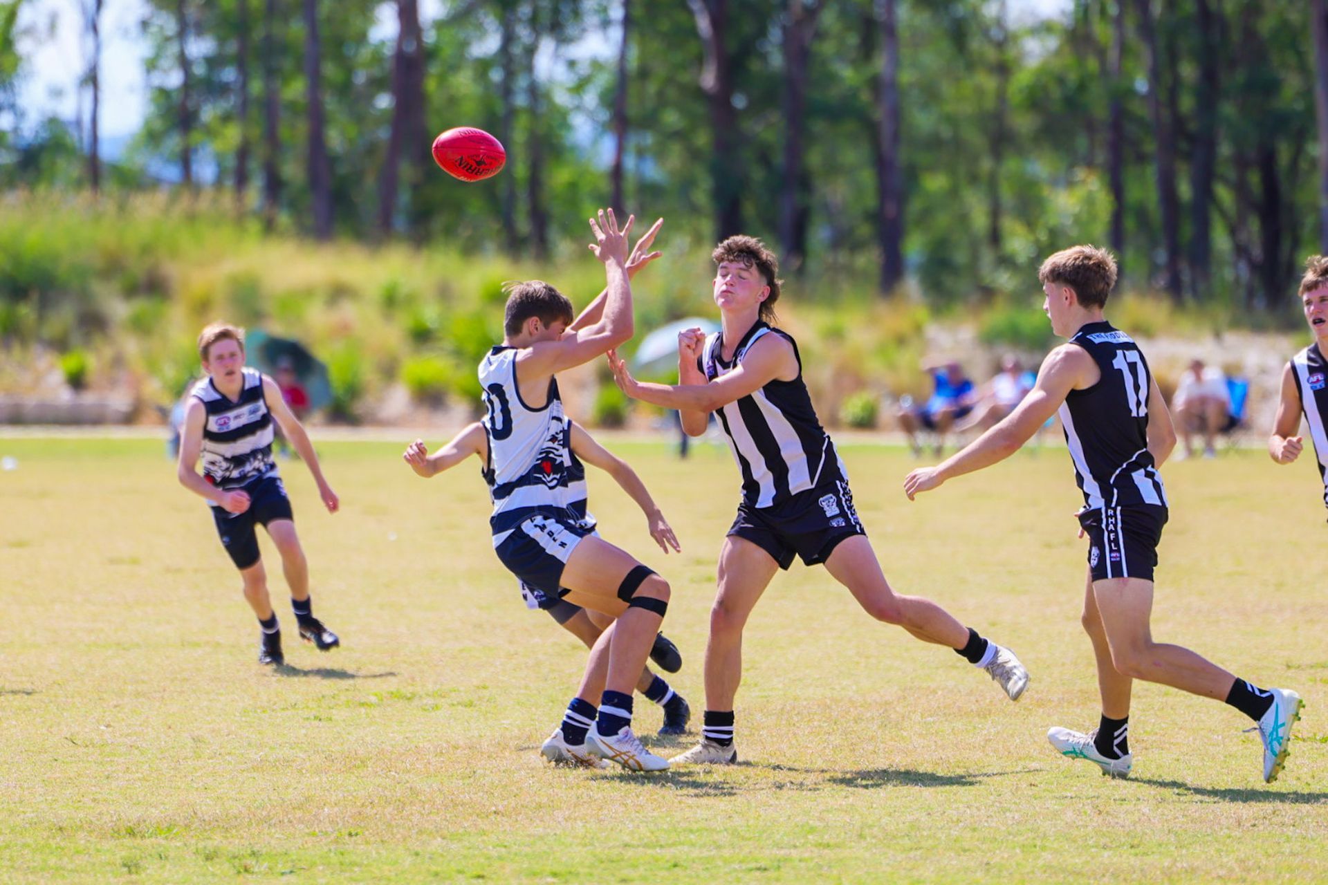 Australian rules football players in black and white uniforms on a grassy field, one jumping to catch the ball.
