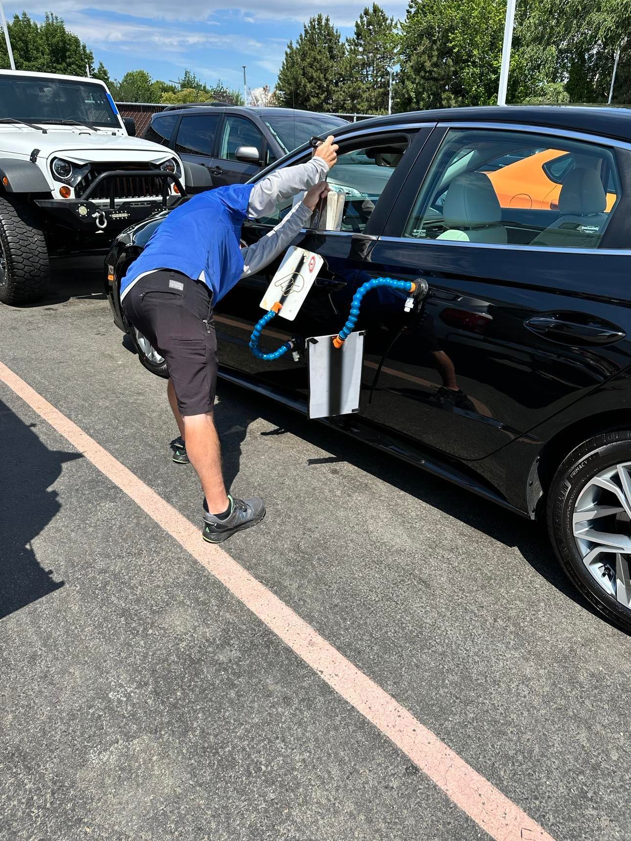 A person using a specialized light tool to perform paintless dent repair on the side of a black car.